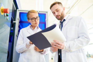 Pretty blonde-haired technician and her bearded colleague studying operation manual of modern equipment while standing at production department of dairy plant